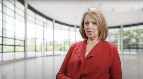 Photo of Brenda Lee, CEO of the University of Toledo Foundation, being interviewed. She is a blond woman wearing a red shirt, sitting in a room with large windows.